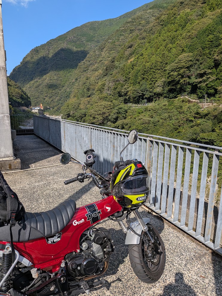 ダムの上の通路に停めたDAX125とヘルメット。奥に吉野川上流の渓谷